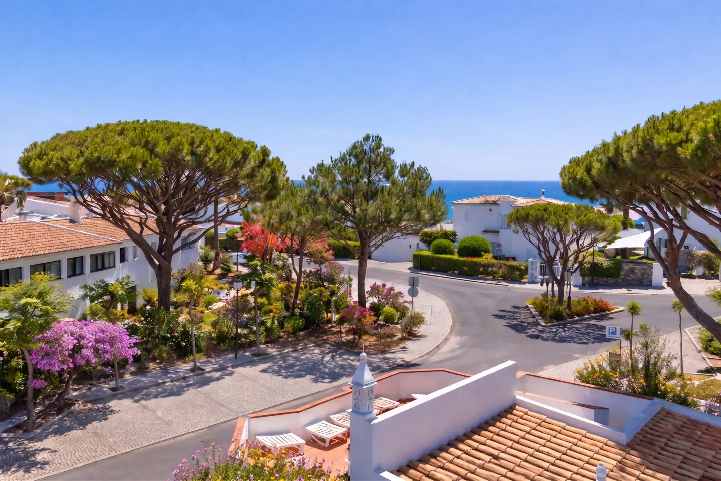 Scenic view of a coastal neighborhood with white houses, lush trees, and a glimpse of the blue ocean under a clear sky.