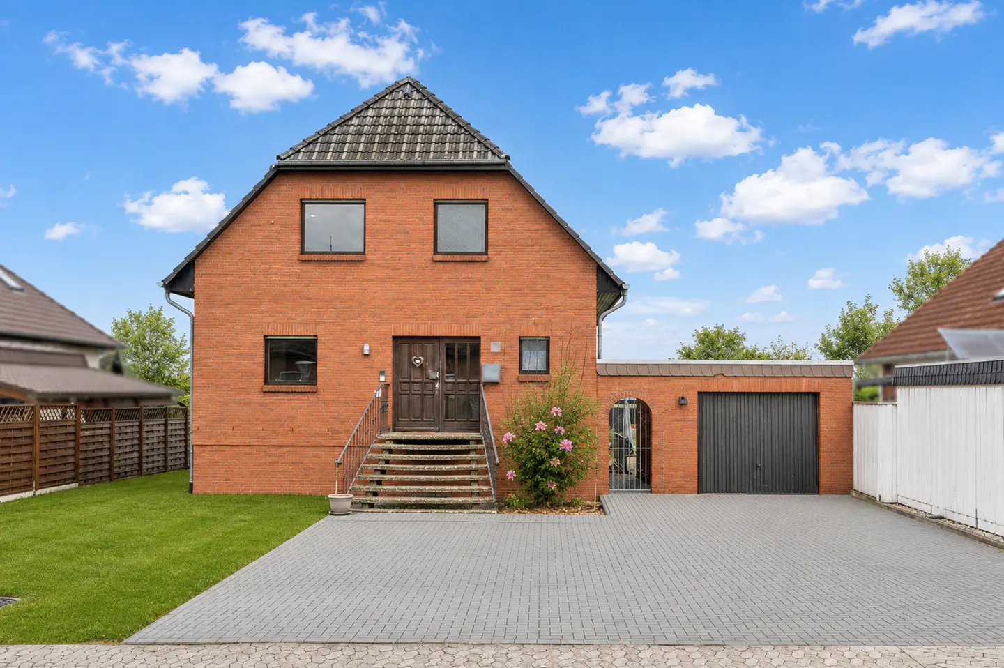 Two-story red brick house with a gray roof, steps leading to the front door, and a gray brick driveway.