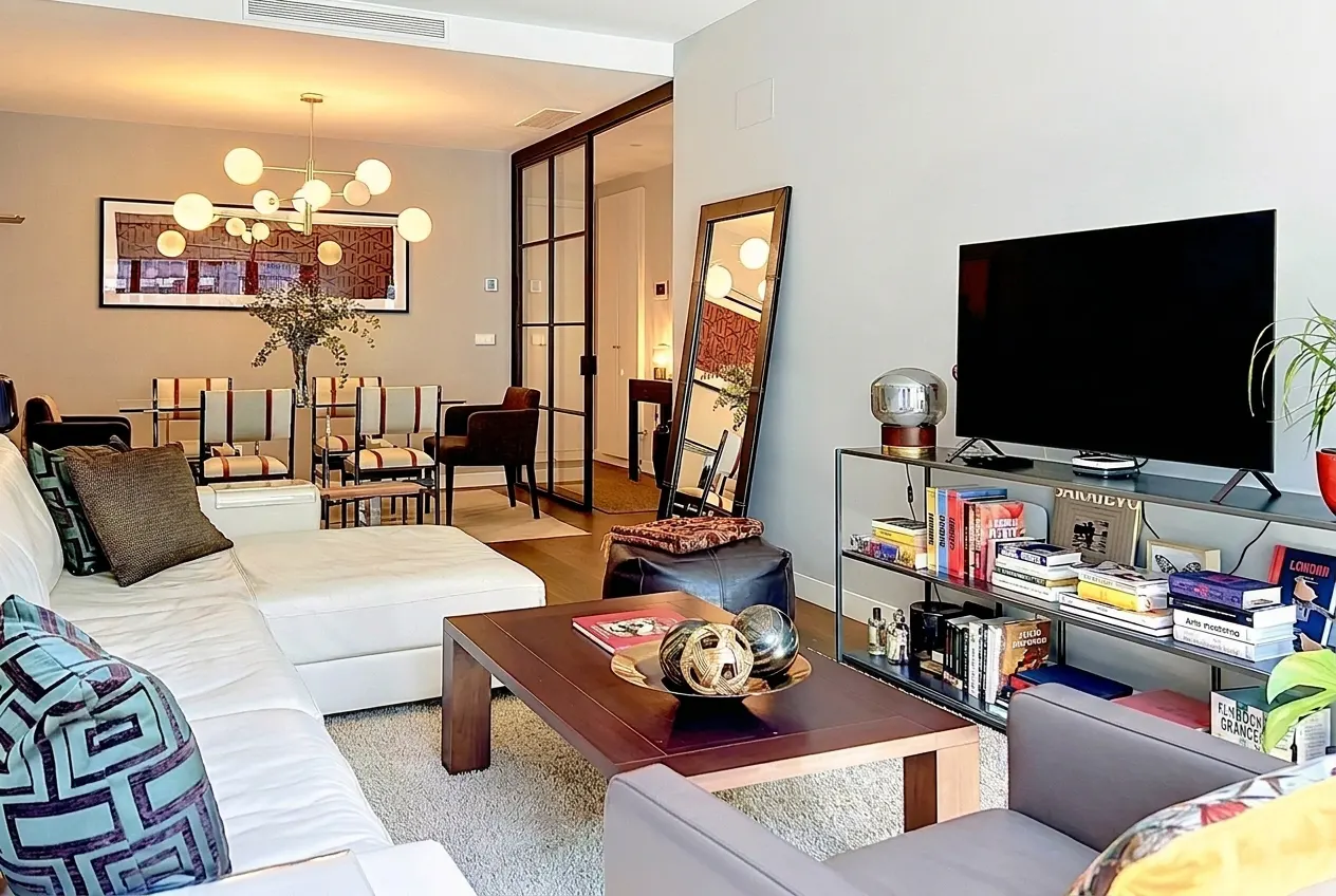 A modern living room with a white sofa, wood coffee table, TV on a metal shelf, and a full-length mirror.