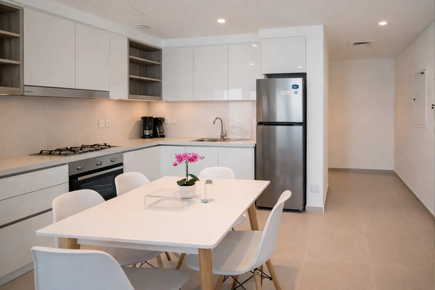Bright, modern kitchen with white cabinets, stainless steel appliances, and a white dining table with pink orchids.