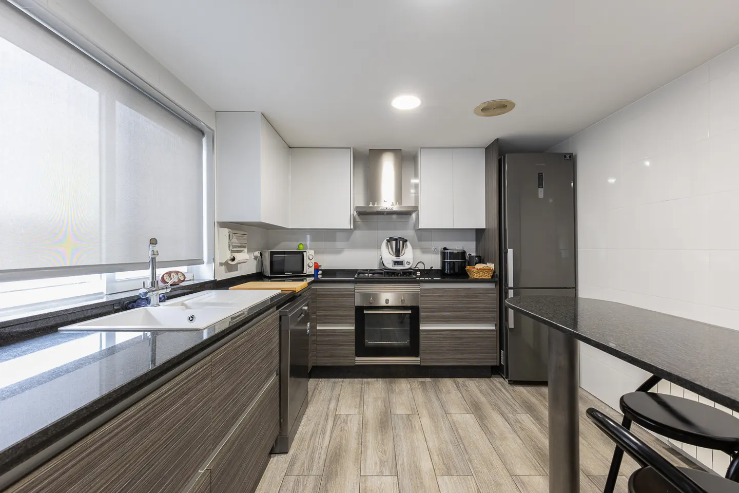 Bright kitchen with white cabinets, gray lower cabinets, stainless steel appliances, and a black countertop island with stools.