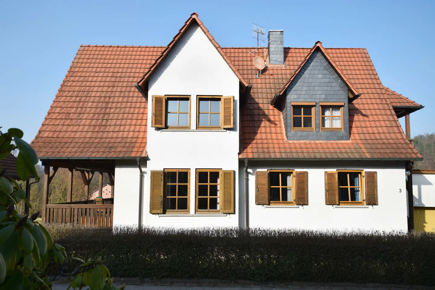 Two-story white house with a red tile roof and brown shutters under a clear blue sky.