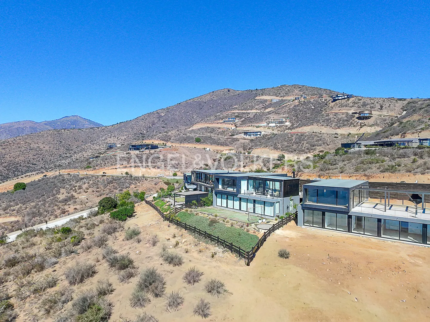 Modern gray house with large windows on a hillside under a clear blue sky.
