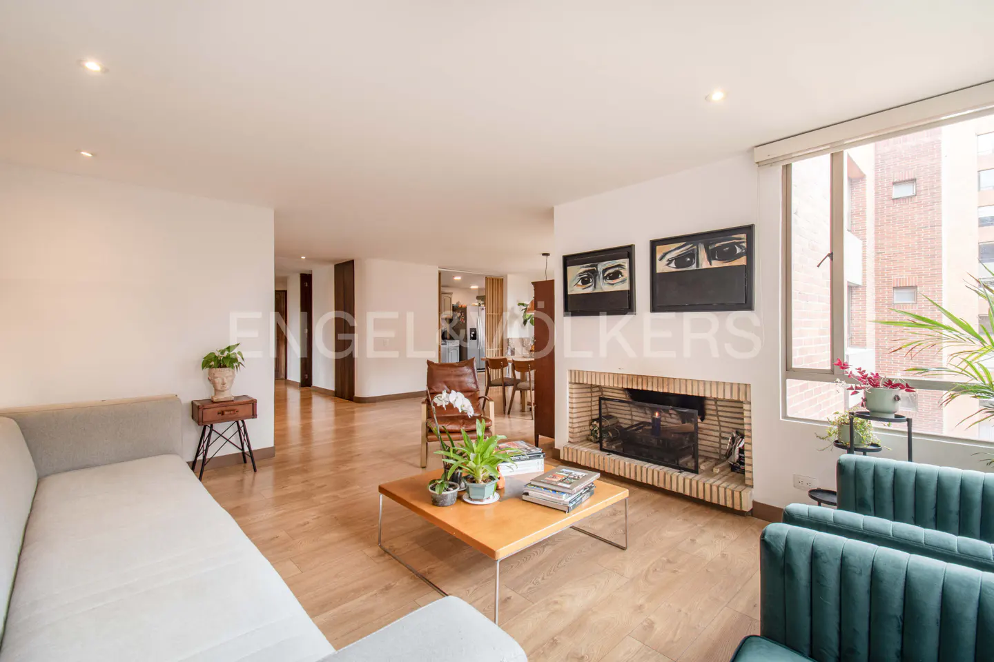 Bright living room with hardwood floors, a gray sofa, a brick fireplace, and a large window with a view of a brick building.
