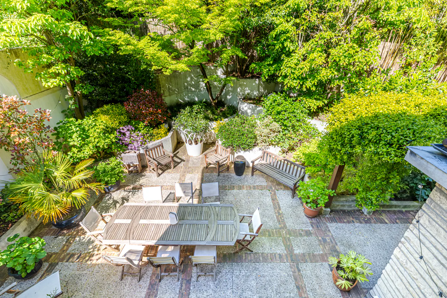 Overhead view of a patio with a wooden table, chairs, bench, and lush green plants.