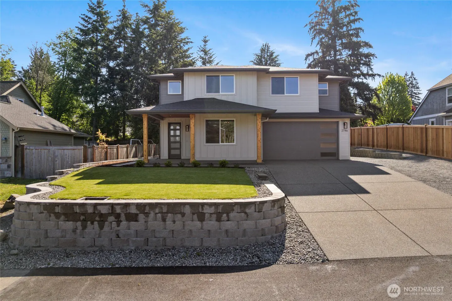 Two-story home with gray siding, a dark gray garage door, and a green lawn. The house has a covered porch with wooden pillars.