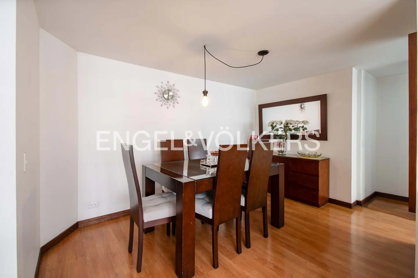 Dining room with a wood table, six chairs, wood floors, and a modern light fixture. A sideboard with a mirror is against the wall.