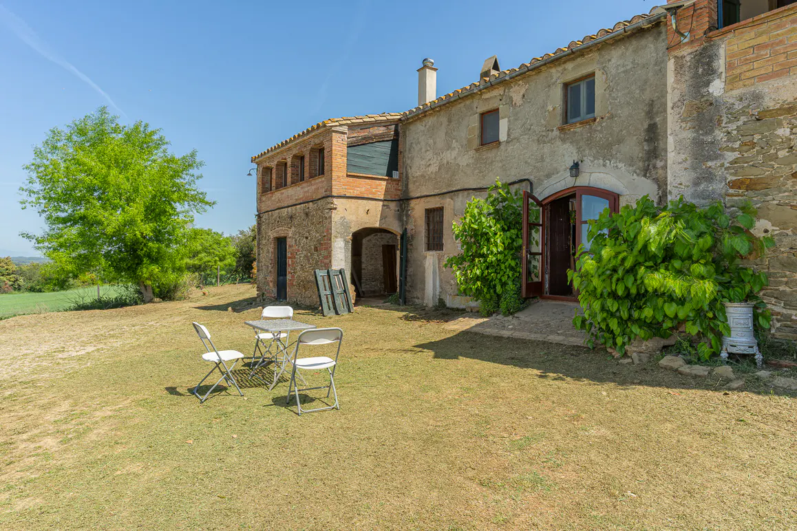 Exterior of a stone farmhouse with a table and chairs on the lawn. The front door is open.