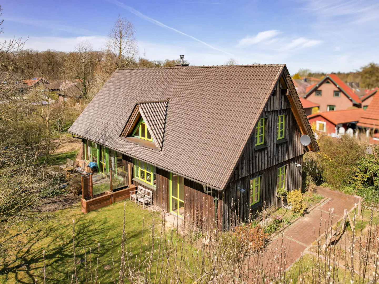 Two-story wood house with a brown roof and green trim, surrounded by trees and a brick path.