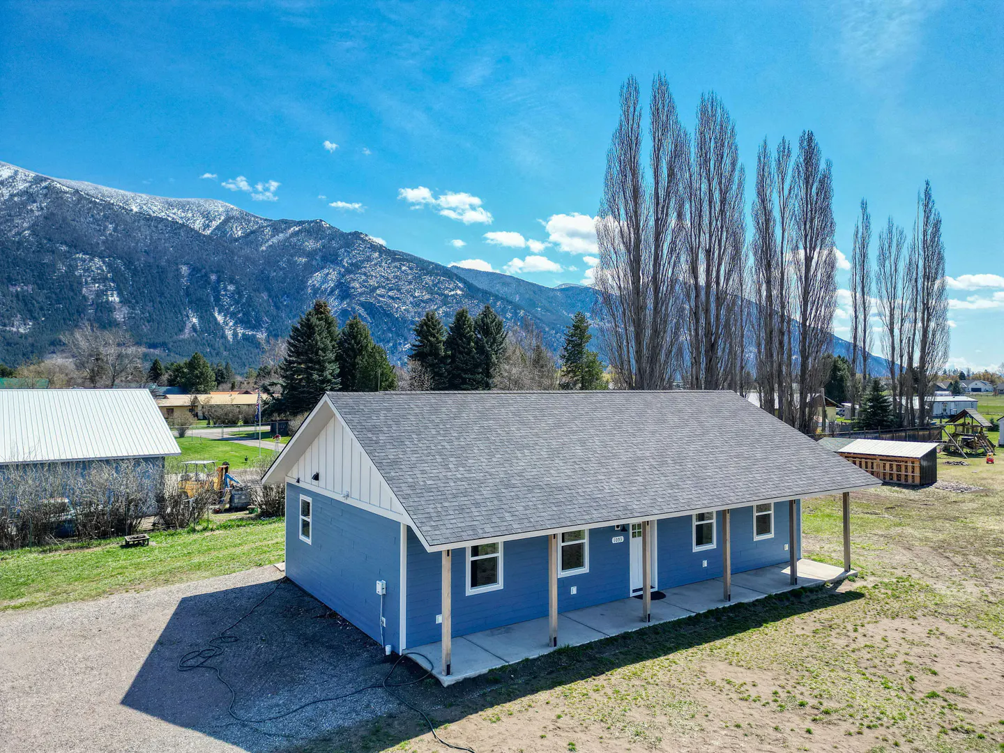 Blue house with a gray roof and a mountain backdrop on a sunny day.