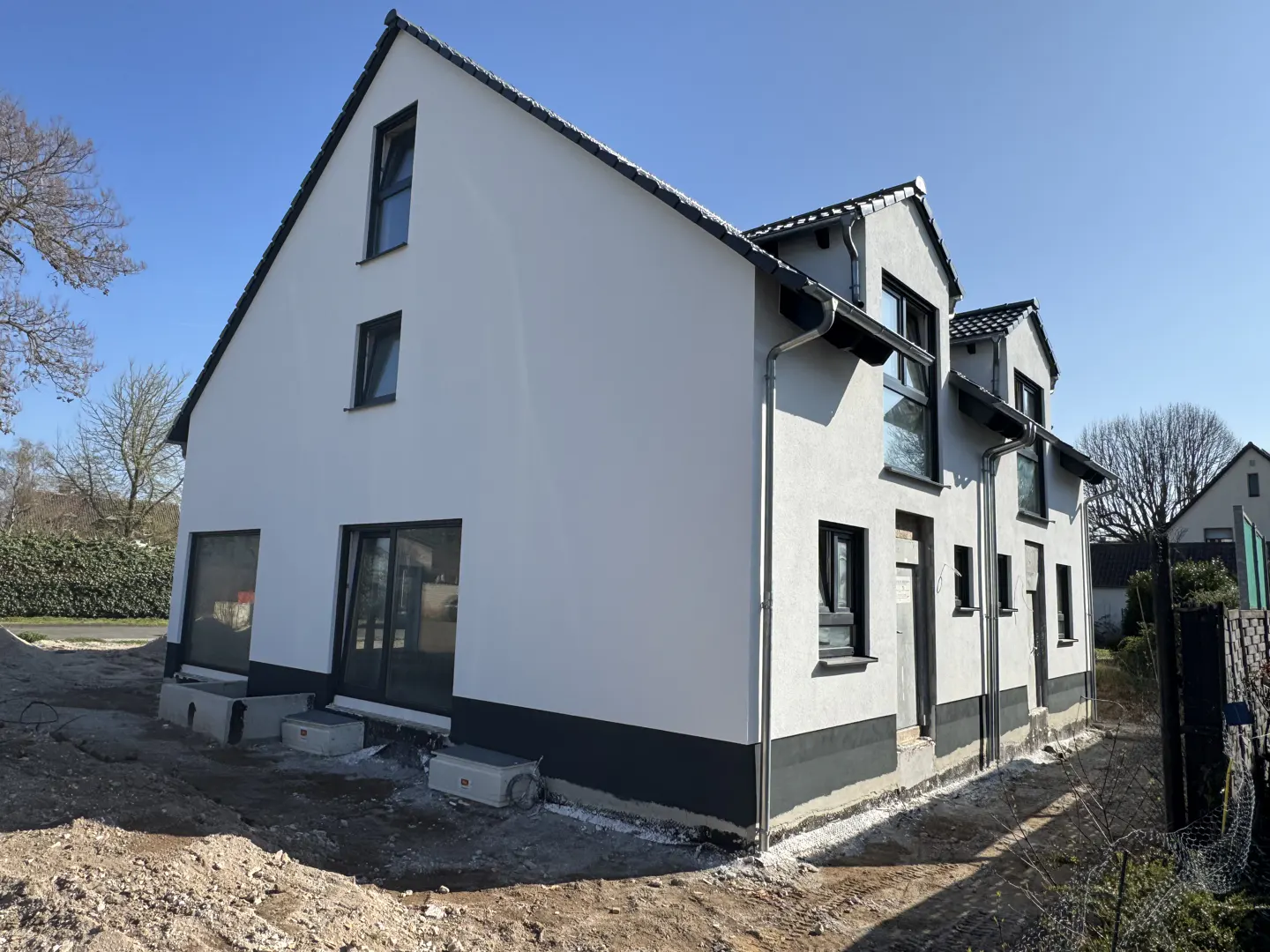 Two-story white house with black trim and windows, under a clear blue sky. Construction site with dirt in the foreground.