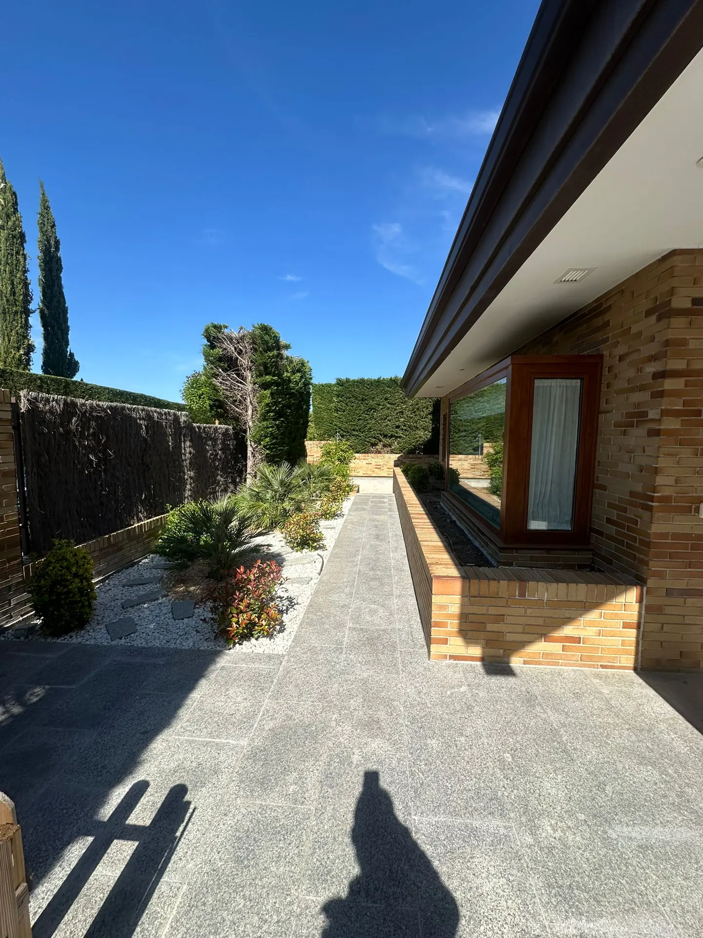 Exterior view of a brick house with a stone walkway, garden, and blue sky.