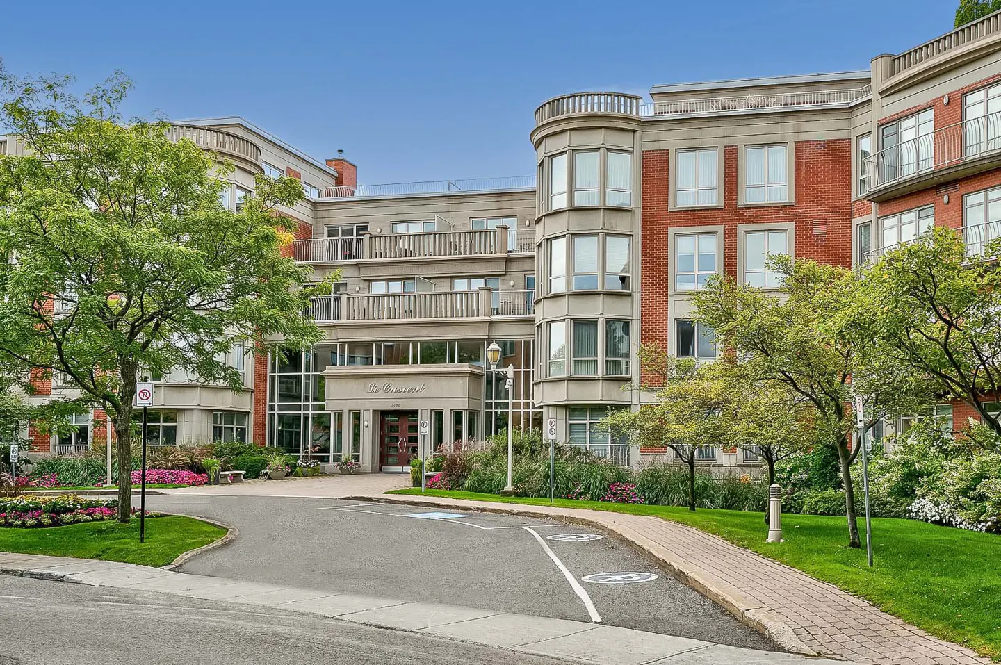 Exterior view of a multi-story brick and concrete apartment building with a circular driveway and green trees.