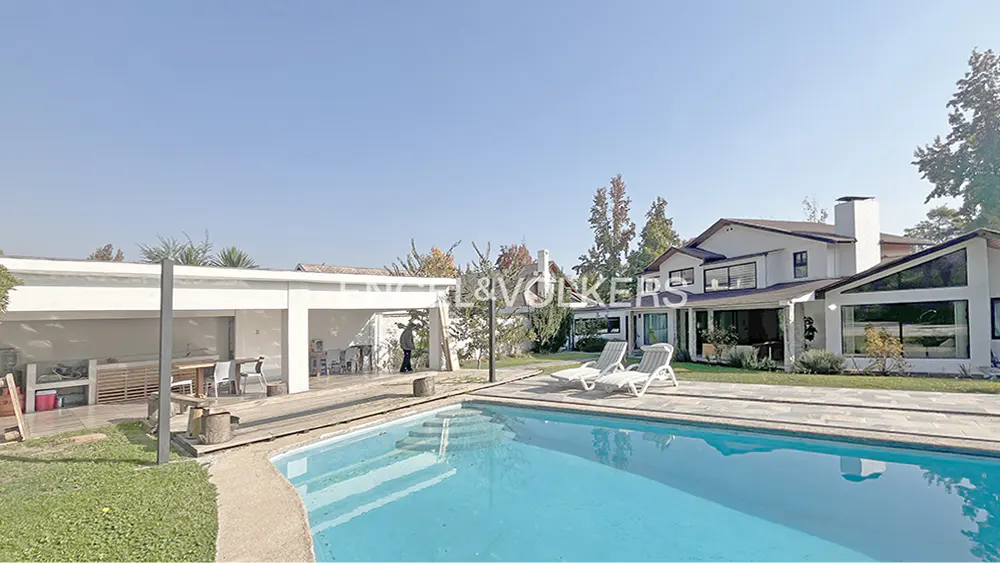 Exterior view of a white house with a pool, lounge chairs, and a covered outdoor kitchen area.