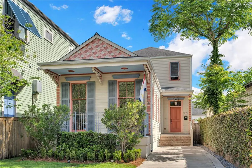 Two-story house with a porch, blue shutters, and a salmon-colored door. A New Orleans flag is displayed on the porch.