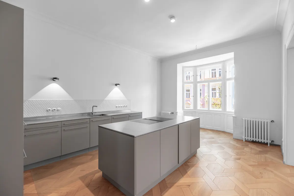 Bright, modern kitchen with gray cabinets, island, and herringbone wood floors. Large bay window lets in natural light.