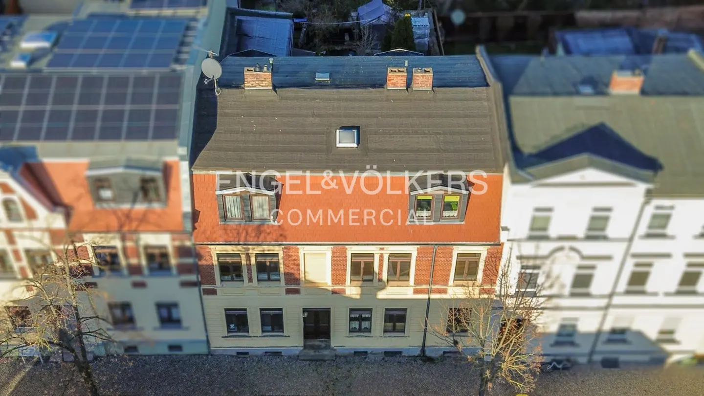 Aerial view of a three-story building with a black roof and red brick facade, Engel & Volkers logo on the building.