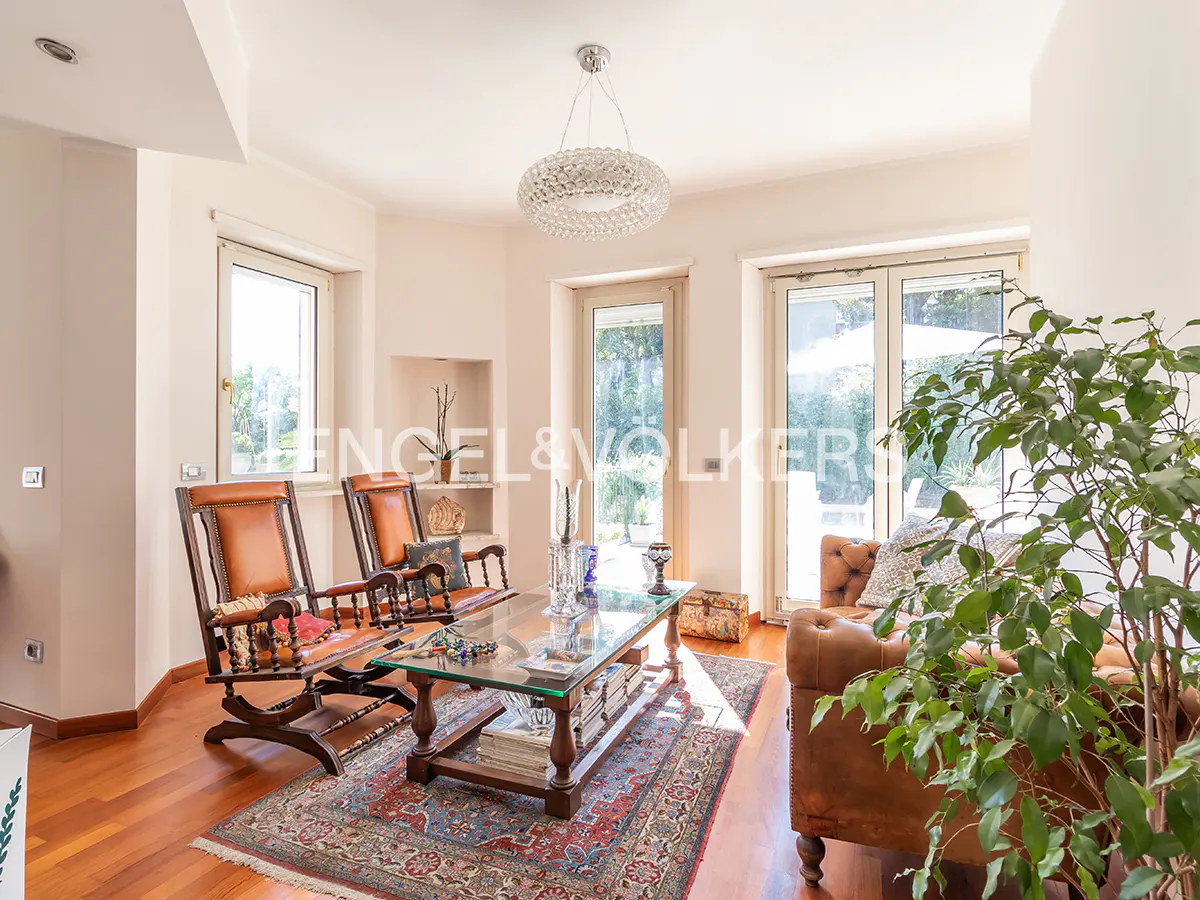 Bright living room with two wooden rocking chairs, a glass coffee table, a leather sofa, and a large indoor plant.