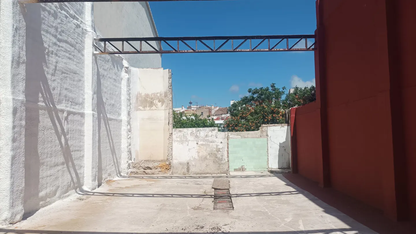 Exterior view of a concrete patio with white and red walls, and a metal beam overhead. A view of buildings and blue sky is visible beyond the walls.