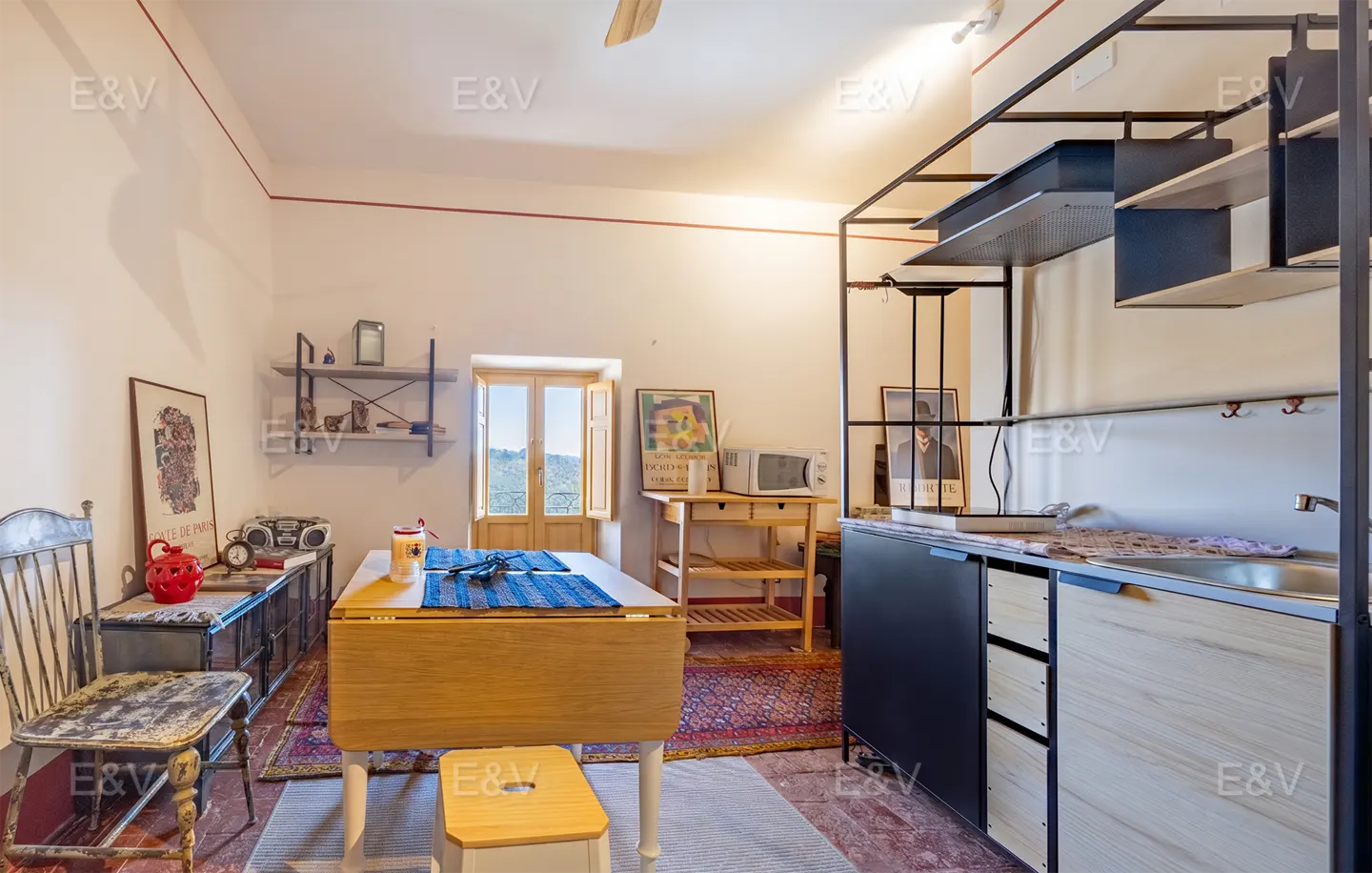 A bright studio apartment with a dining table, kitchenette, and vintage decor.