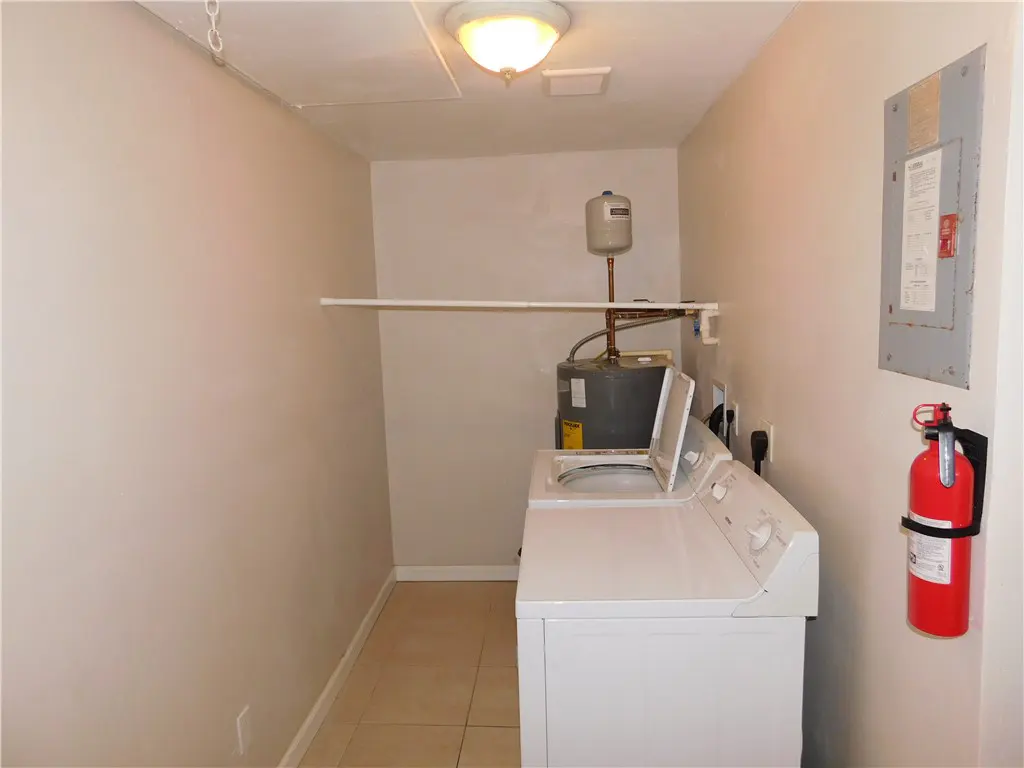 Laundry room with white washer, water heater, and red fire extinguisher on a beige wall.
