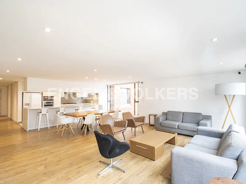 Open-concept living space with wood floors, gray sofas, and a modern kitchen with a white island and dining table.