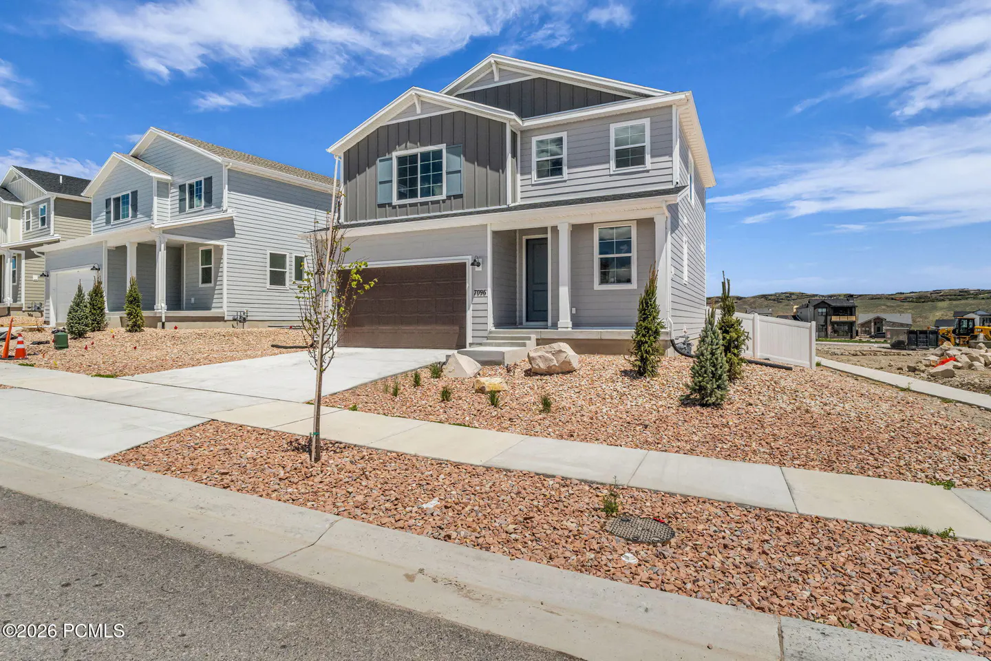 Two-story gray house with a brown garage door, white trim, and a rock garden under a blue sky.