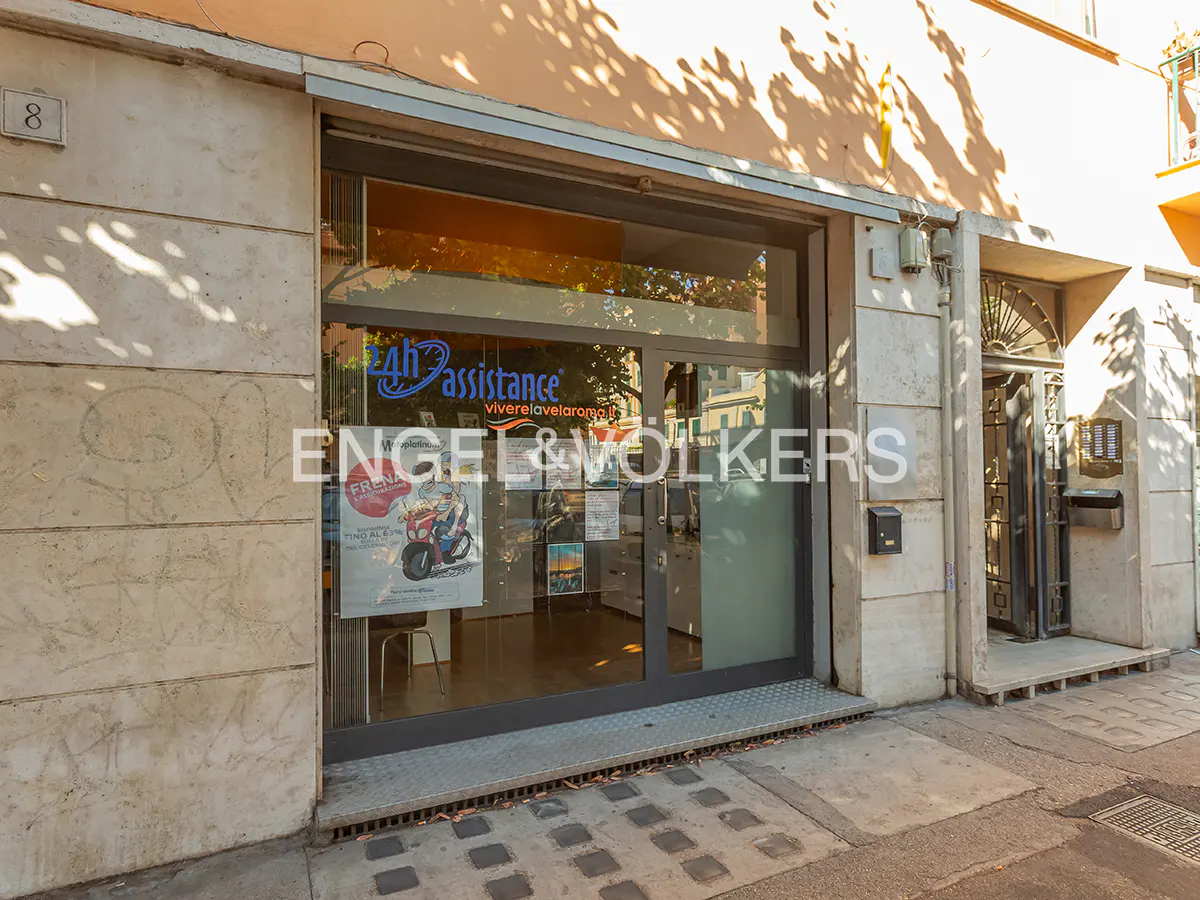 Exterior view of Engel & Volkers real estate office with glass door and posters. A metal grate is in front of the entrance.