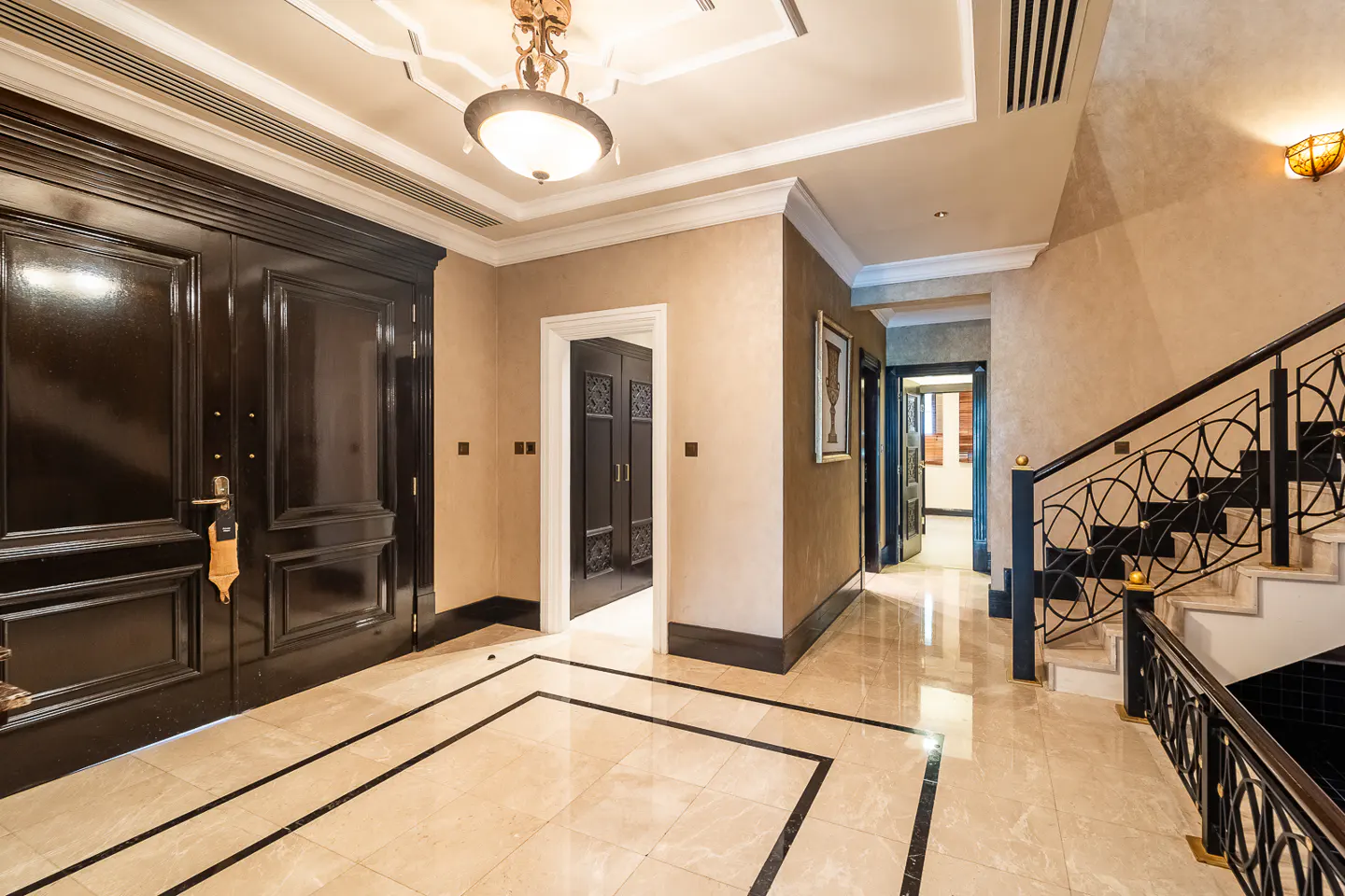 A foyer with marble floors, black doors, and a staircase with black iron railings. A chandelier hangs from the ceiling.
