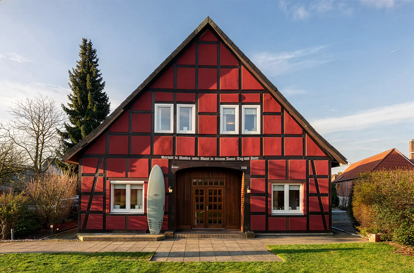 Red half-timbered house with a surfboard leaning against the wall. The house has white windows and a dark wood door.