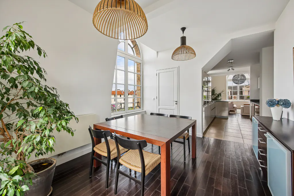 Dining area with a wooden table, black chairs with woven seats, a large potted plant, and two modern dome pendant lights.