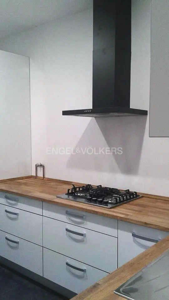 A modern kitchen with white cabinets, wood countertops, a black range hood, and a gas stovetop.