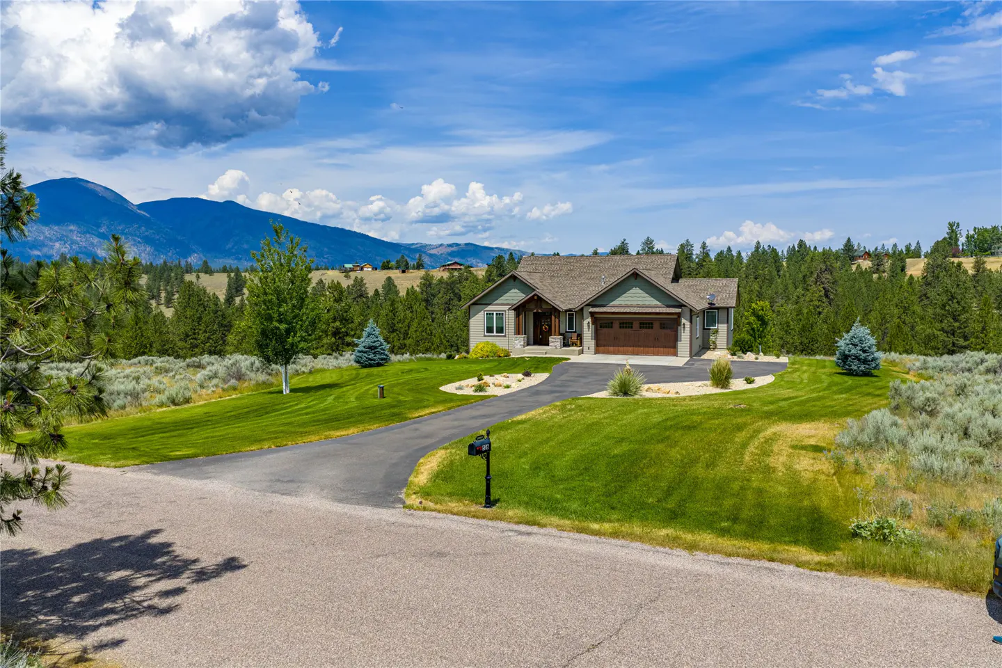A single-family home with a green lawn, a driveway, and mountains in the background.