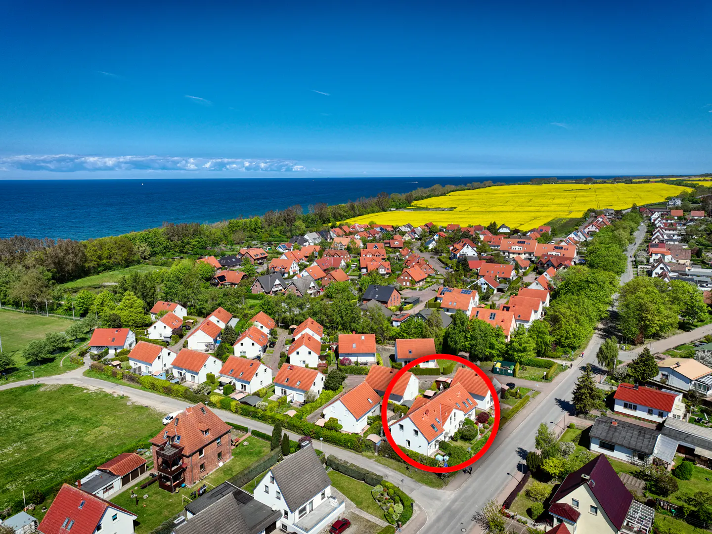 Aerial view of a coastal town with white houses and red roofs, near a yellow field and blue sea, circled in red.