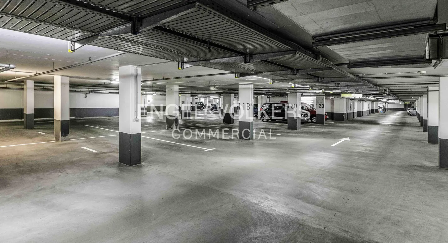 Indoor parking garage with concrete floor, white parking lines, and gray and white support columns.