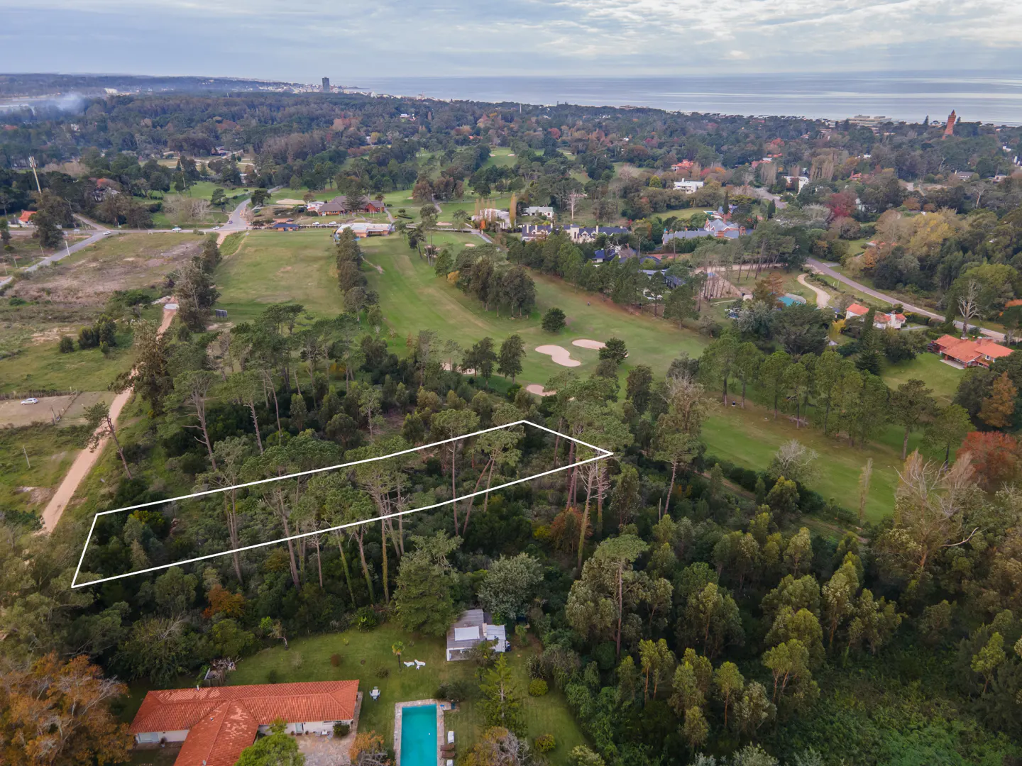 Aerial view of a wooded property outlined in white, near a golf course and the ocean.