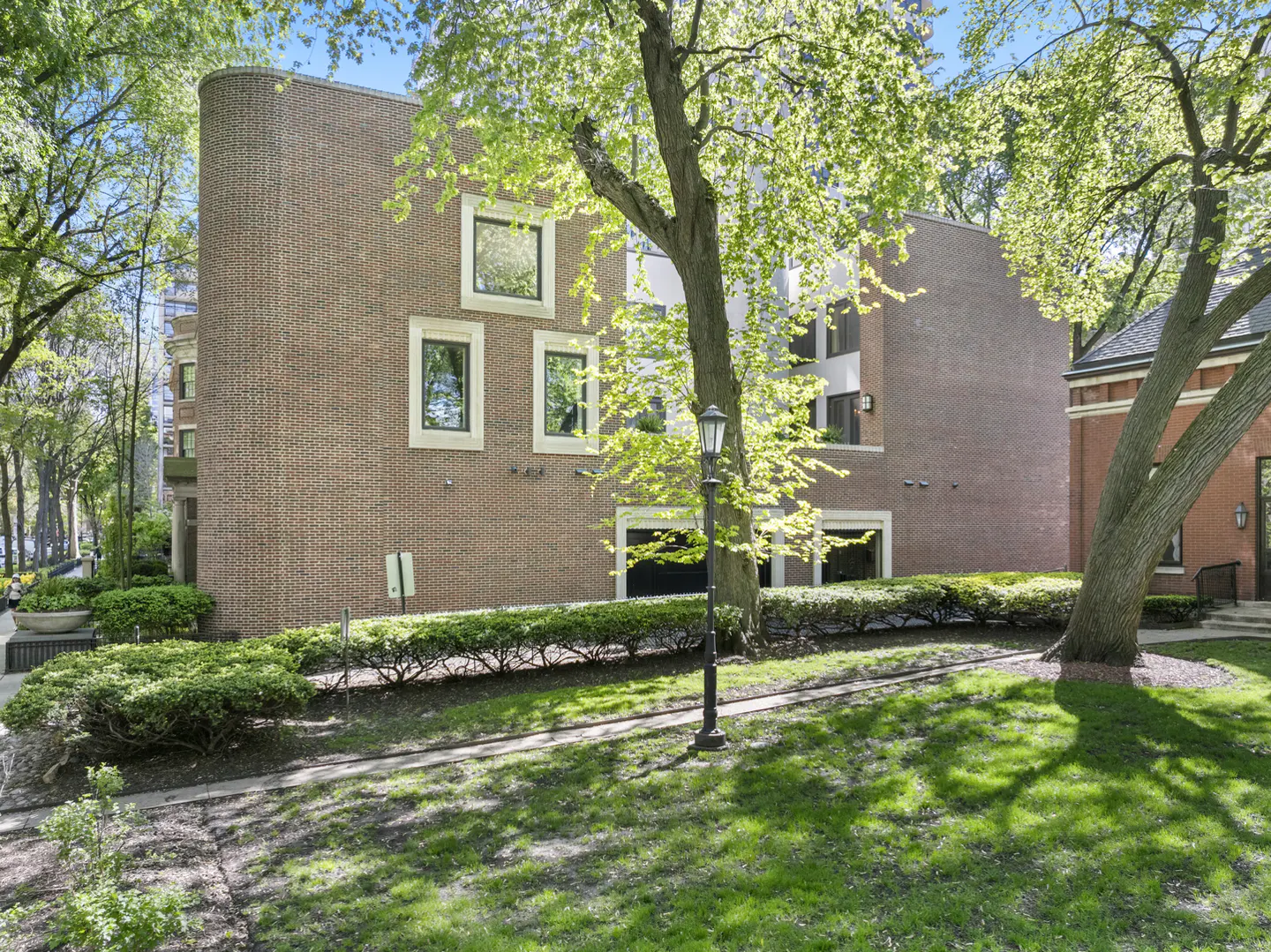 Brick apartment building with square windows, green lawn, and trees. A black lamppost stands in front of the building.