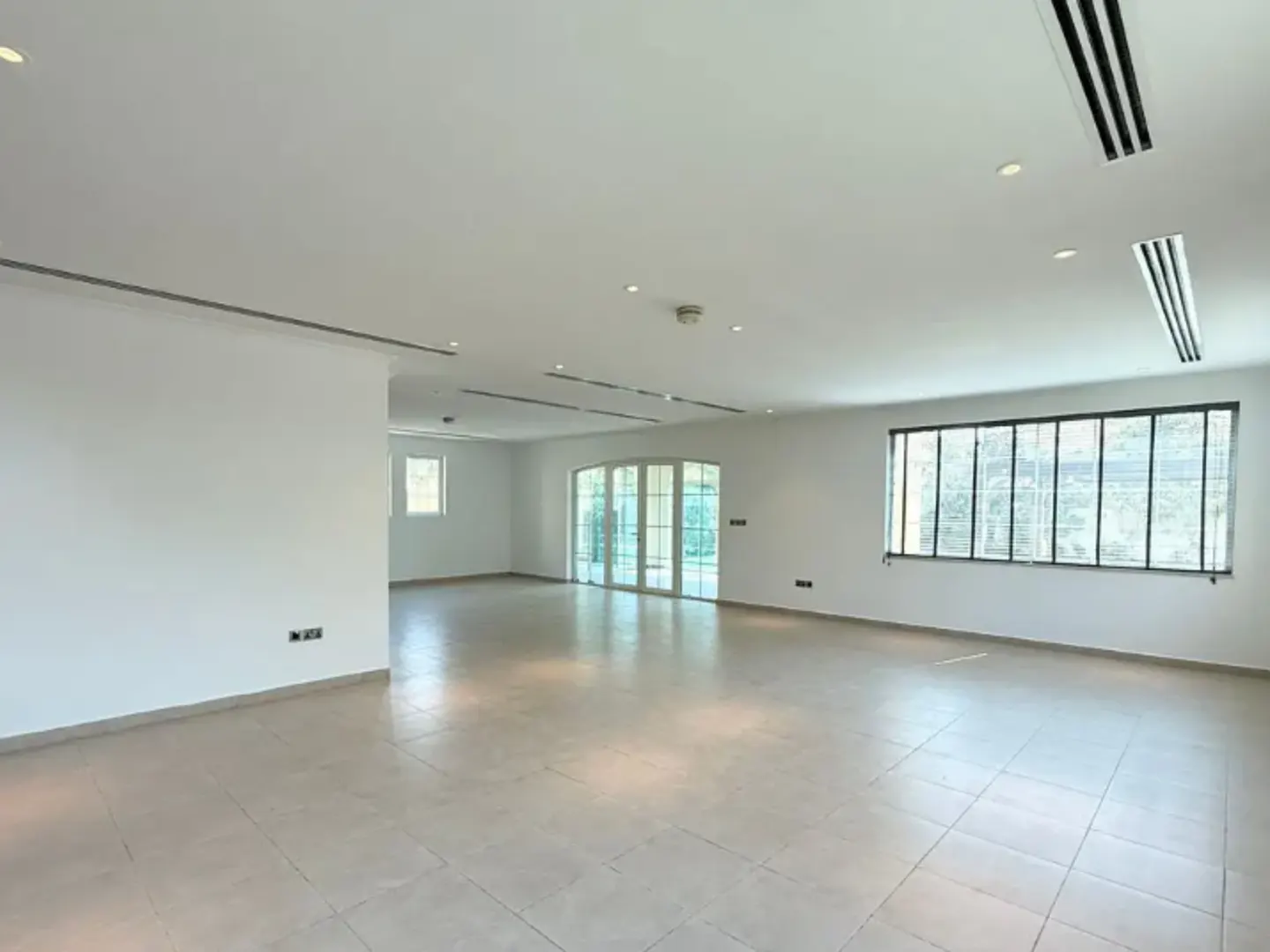 Bright, empty room with white walls, tile floor, and large windows. Natural light floods the space.