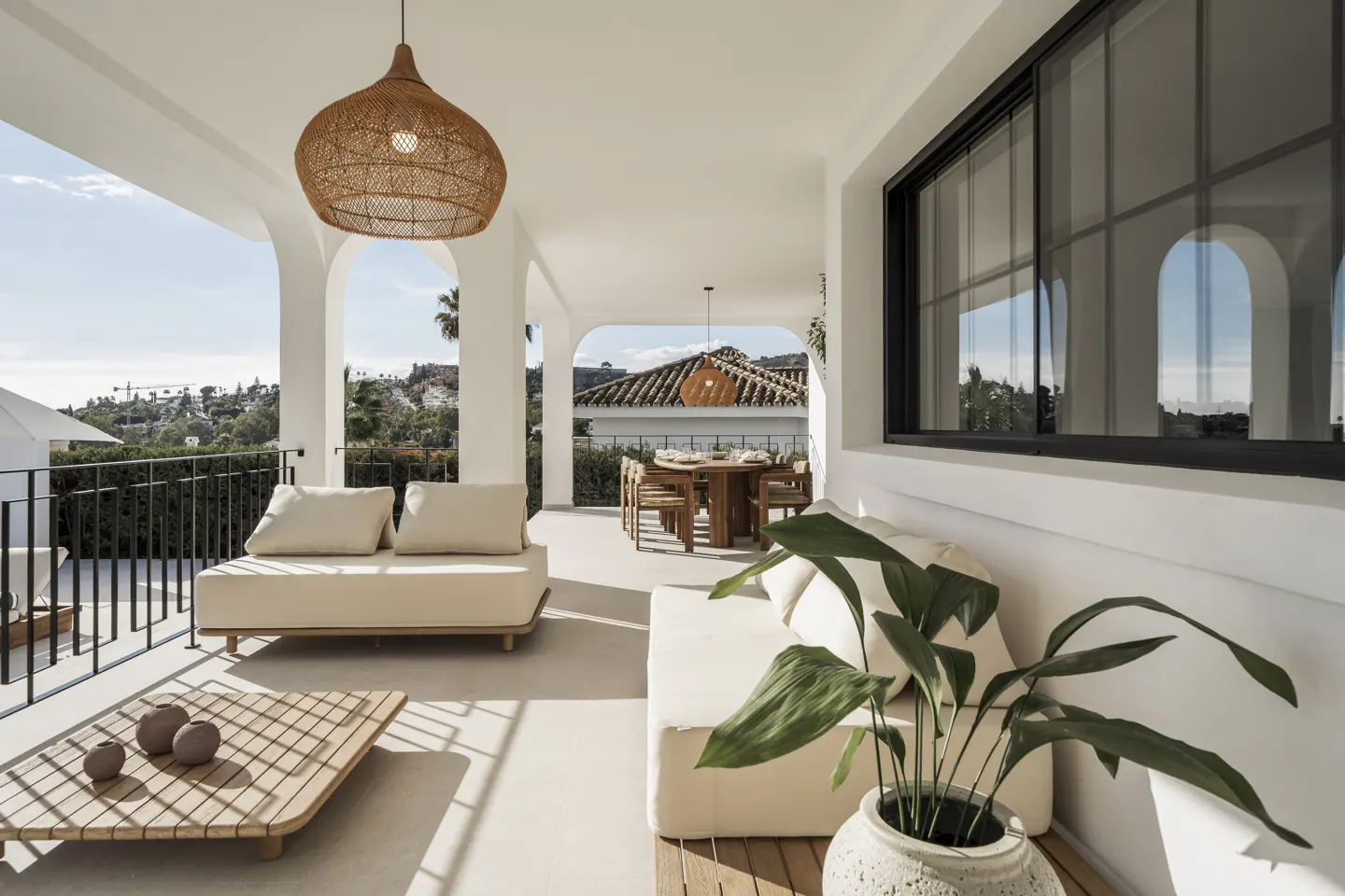 Covered patio with white arches, wicker pendant light, and outdoor furniture. A dining table is visible in the background.