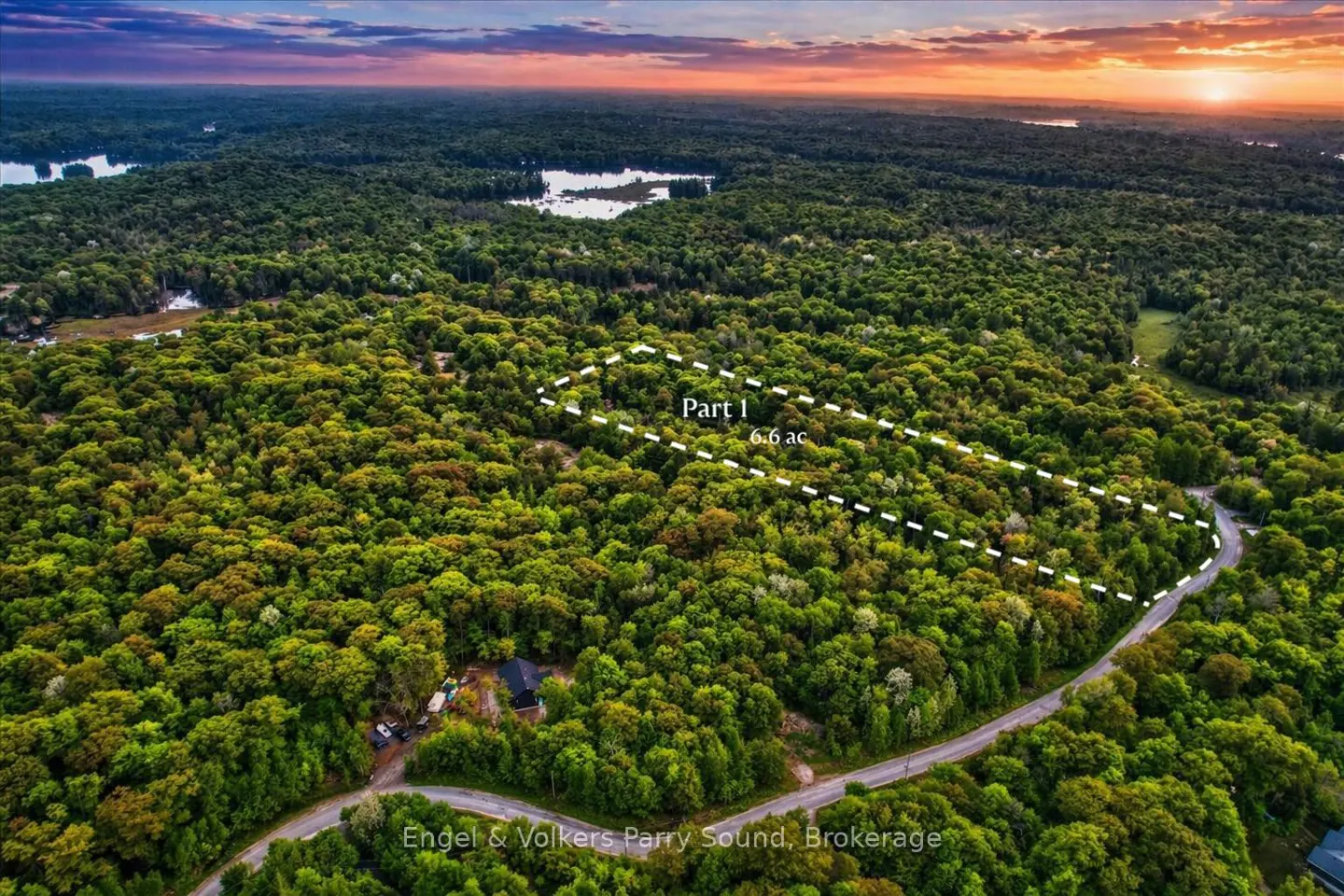 Aerial view of a 6.6 acre wooded property outlined in white, with a road and a glimpse of a house. Sunset sky.