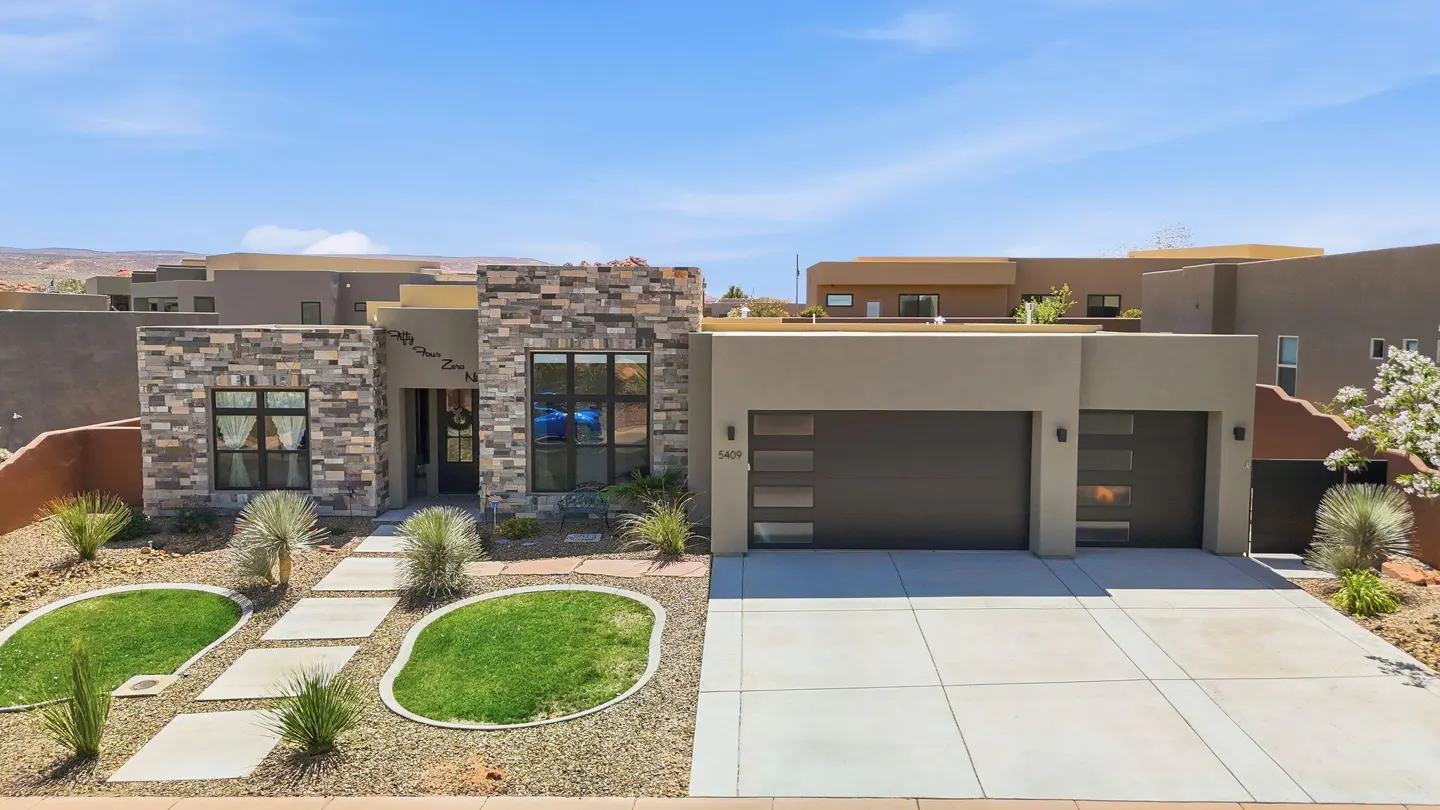 Tan modern home with stone accents, a two-car garage, and a concrete driveway under a blue sky.