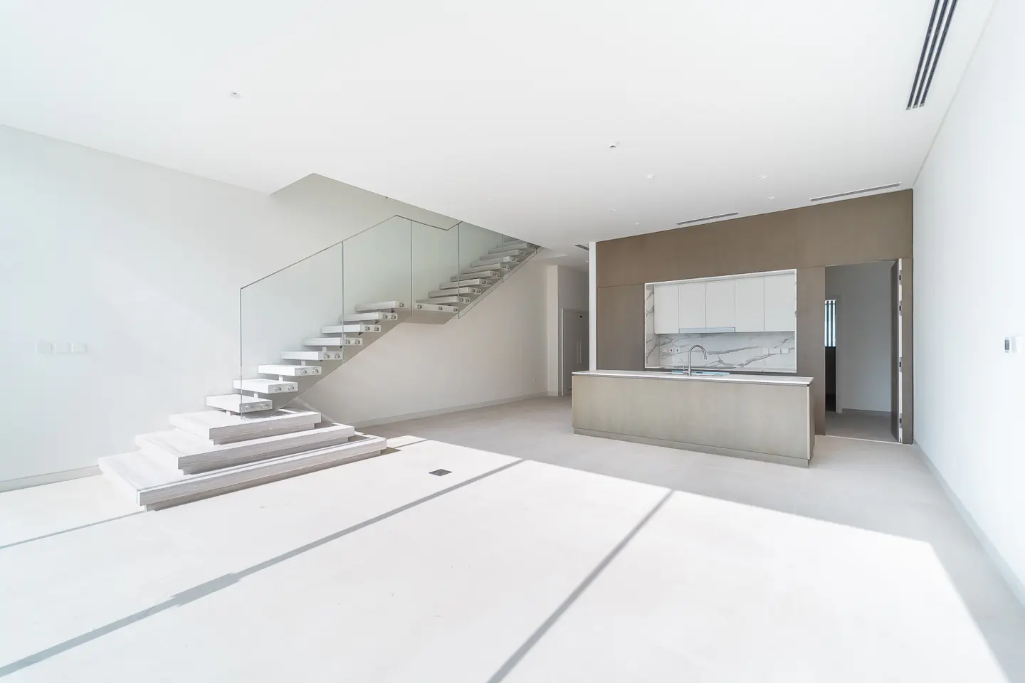 Bright, modern home interior with white walls, floating stairs with glass railing, and a kitchen area with white cabinets.