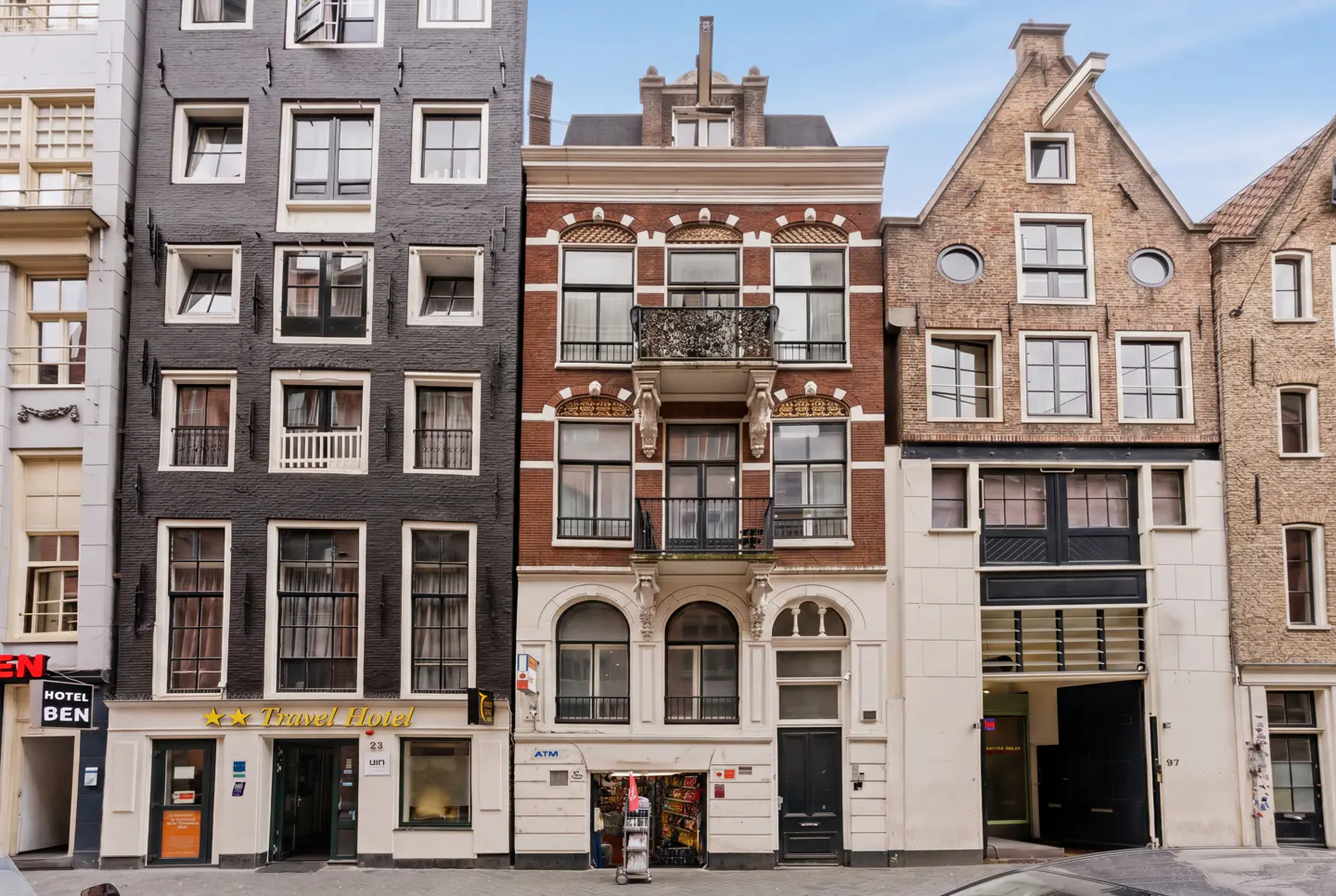 Street view of narrow, multi-story buildings in Amsterdam. Buildings are brick and painted in black, red, and brown. Some have balconies.