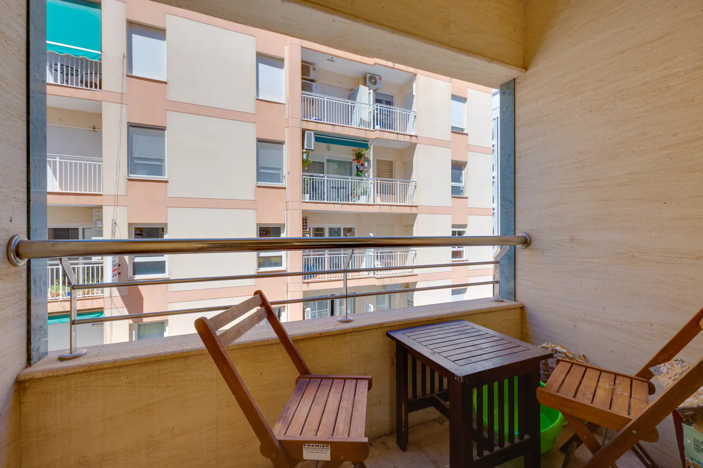 Balcony view with two wooden chairs and a small table, overlooking a multi-story building with balconies.