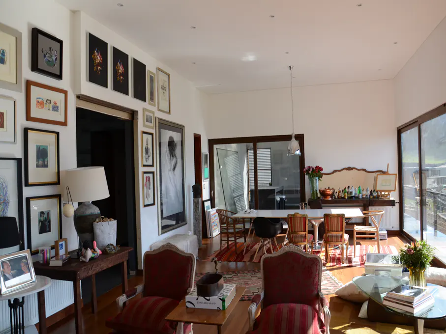 Bright living room with hardwood floors, white walls, and a gallery wall. Dining table and chairs are visible in the background.