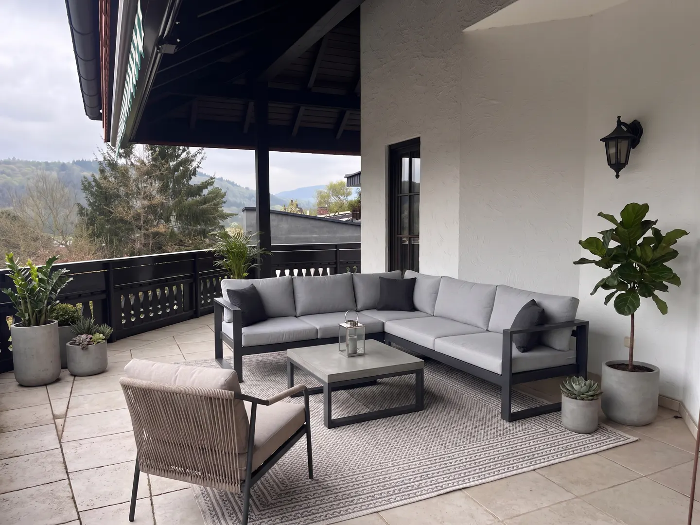 Outdoor patio with gray sectional sofa, chair, coffee table, plants, and a view of the mountains.