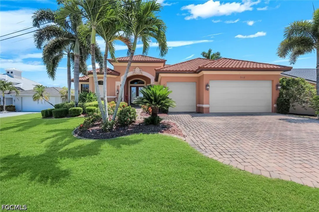 A salmon-colored house with a red tile roof, two-car garage, and palm trees on a sunny day.