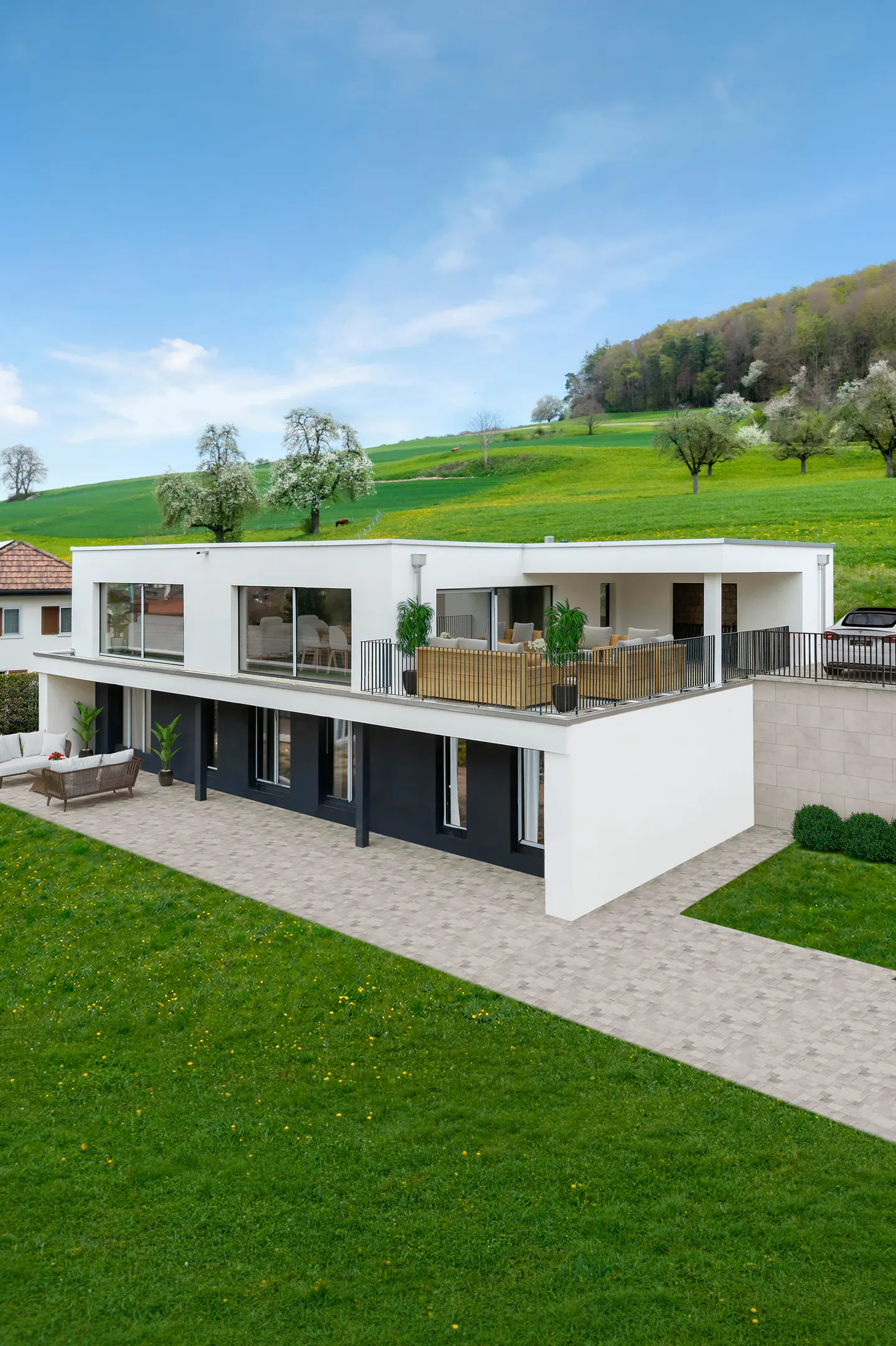 Modern white house with a dark gray base, large windows, and a patio overlooking a green lawn and rolling hills.