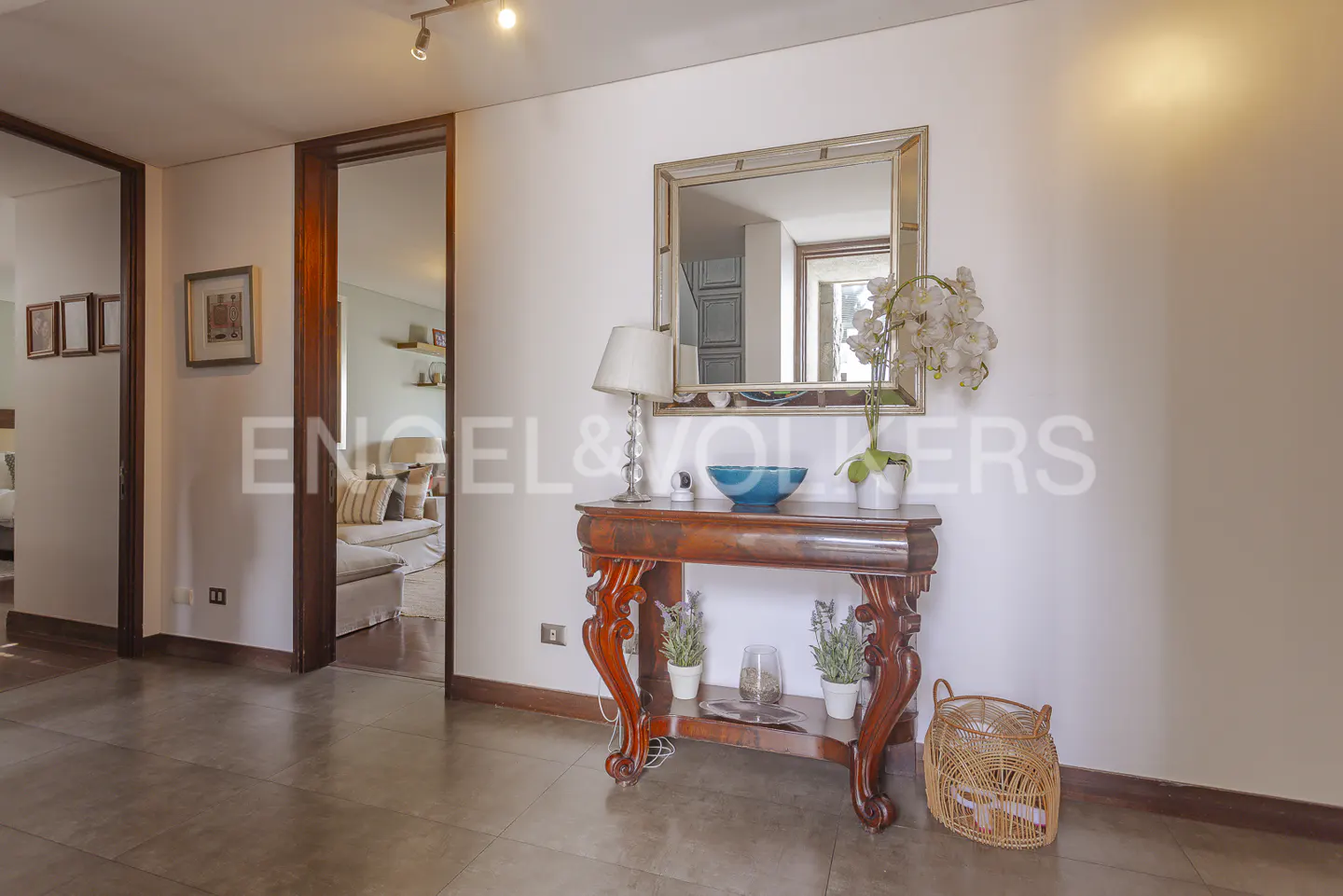 Entryway with a dark wood console table, mirror, lamp, and blue bowl. A doorway leads to a living room with a sofa.