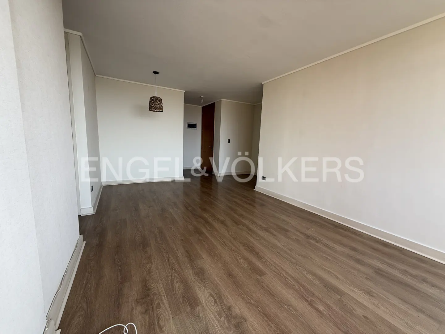 Empty room with wood floors, white walls, and a woven pendant light. Engel & Völkers logo is visible.